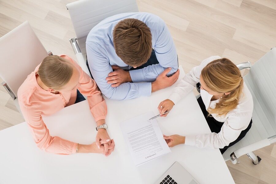 High Angle View Of Female Estate Agent Explaining Document To Young Couple