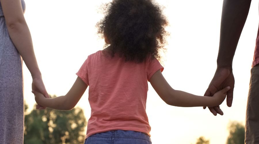 Child holding hands over ears with parents arguing behind him