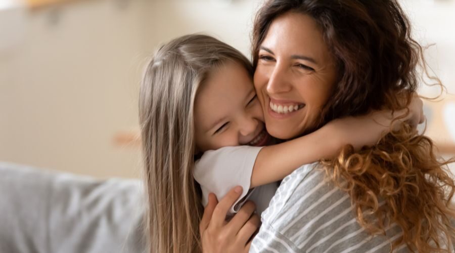 Mother and daughter sitting down hugging and smiling