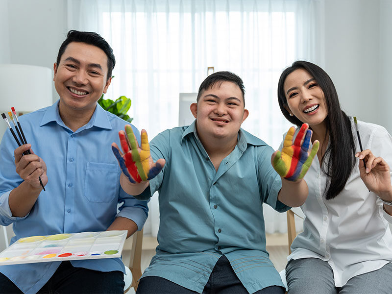 Mother and father sitting down painting with their special needs son