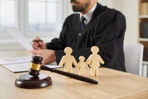 Family of wooden cutouts positioned near a gavel, a judge in the background, illustrating a Richmond family court.