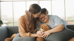 A Tampa mother sitting on a sofa with her arm around her special needs child who is holding a teddy bear.