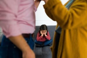 Sad child sitting on a couch, feeling in the middle of her parent's fight about child custody after their divorce.