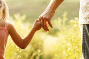 A small child holds her parent's hand while walking through a meadow in Richmond, VA.