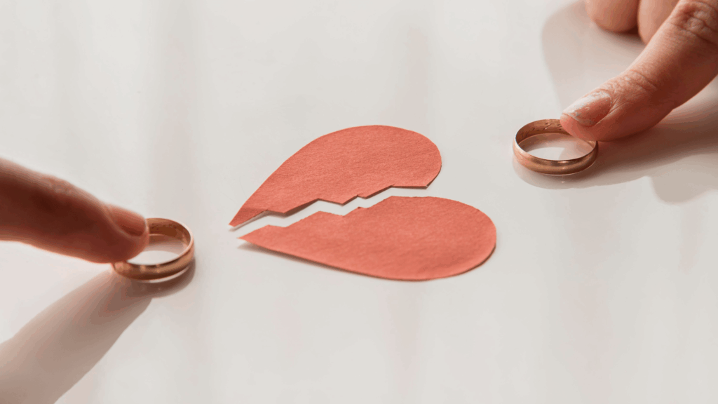 Two fingers pulling wedding rings away from a paper broken heart