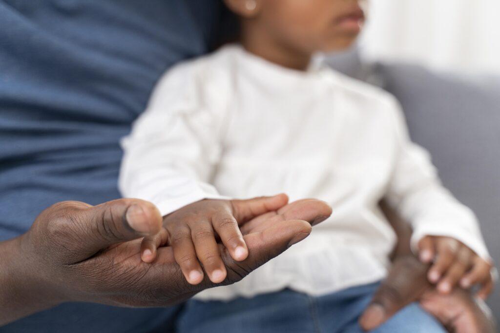 Close-up of a child’s small hand resting in an adult’s open palm, symbolizing care and support.